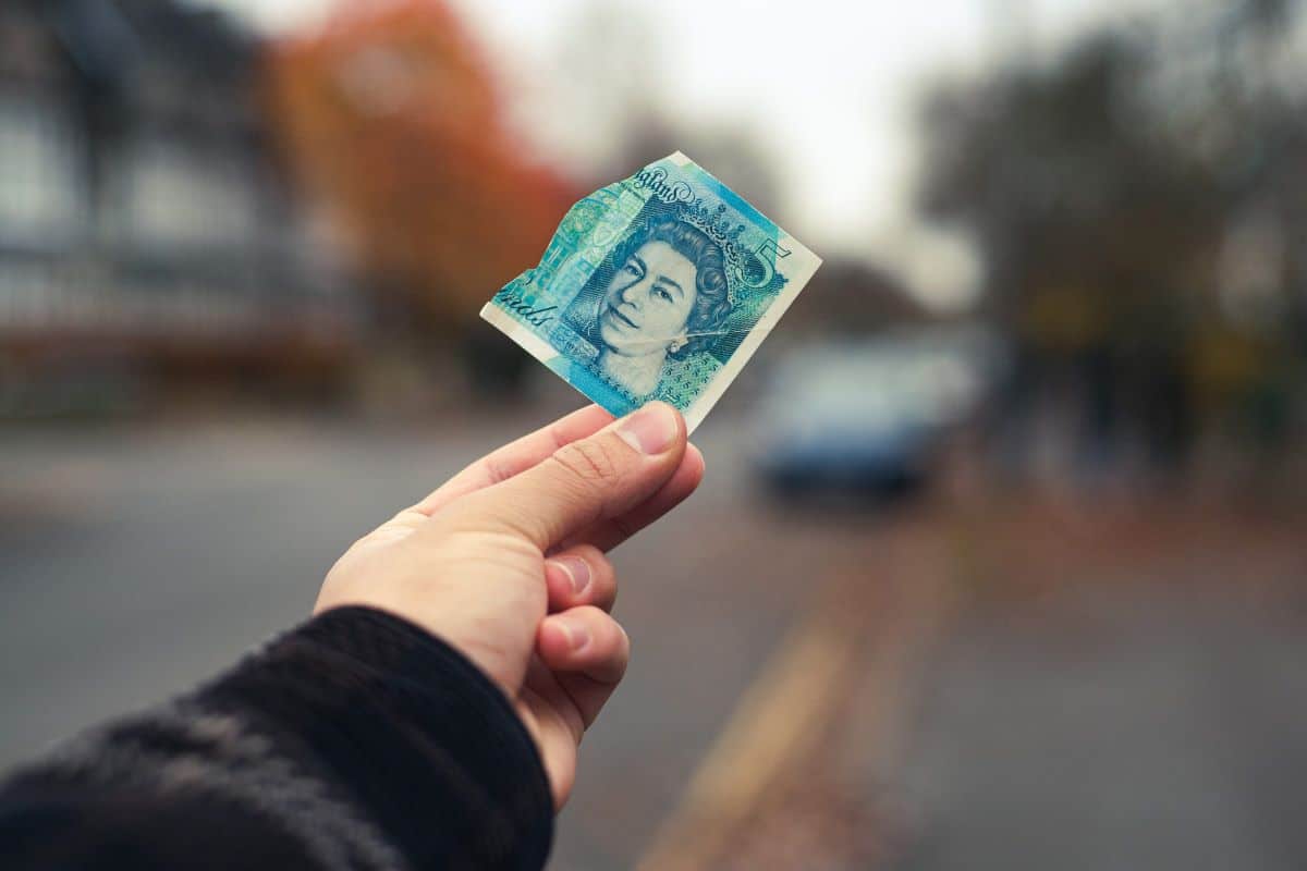 A £5 note being held by out by somebody's hand on a quiet street